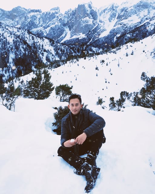 Mark sitting in the snow with mountains behind him